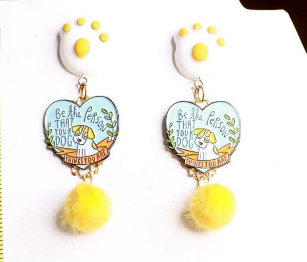 A pair of earrings with yellow pom poms and a heart shaped charm.