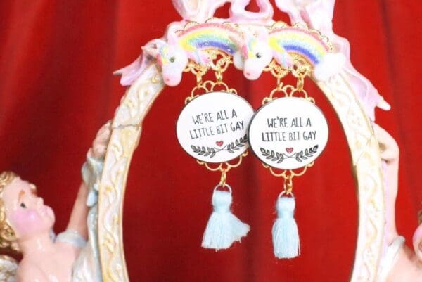 A pair of earrings with the words " we 're all a little bit gay and a lot of unicorn."