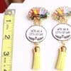 A pair of earrings with yellow tassels and a quote.