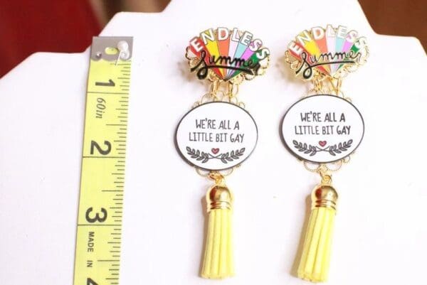 A pair of earrings with yellow tassels and a quote.
