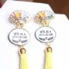 A pair of earrings with yellow tassels and a quote.