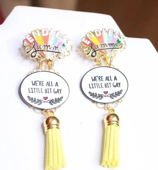 A pair of earrings with yellow tassels and a quote.