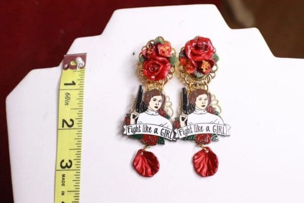 A pair of earrings with red roses and a woman 's face.