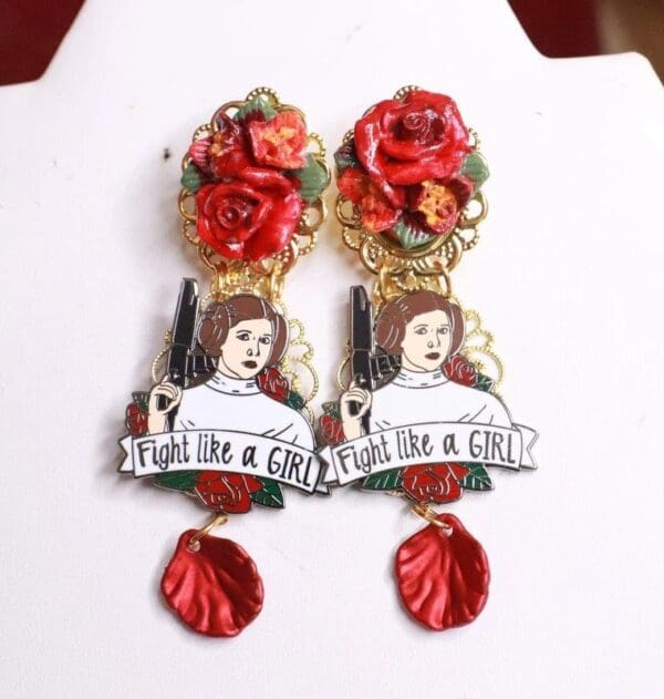 A pair of earrings with red flowers and a woman 's face.