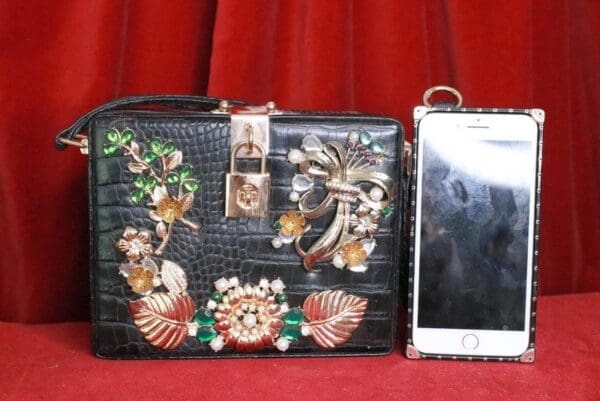 A black purse sitting next to a cell phone.