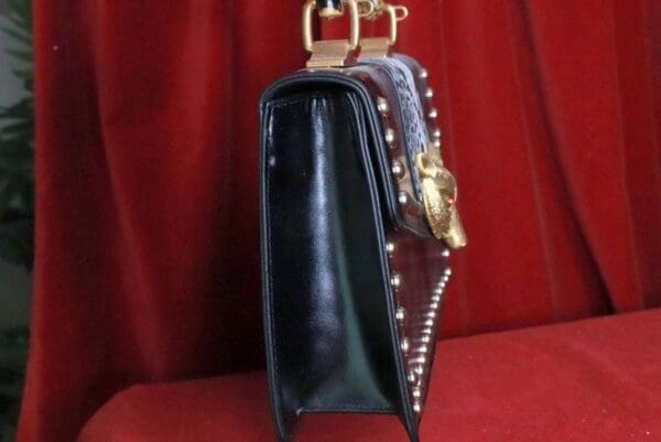 A black purse with gold hardware and a red curtain