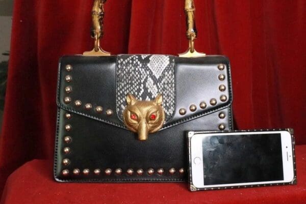 A black purse with gold accents and a phone
