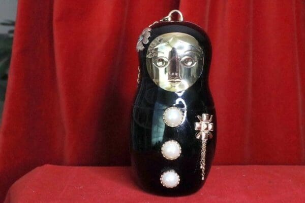 A black russian doll with silver face and cross on top.