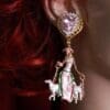 A woman wearing earrings with a picture of a woman and two lambs.