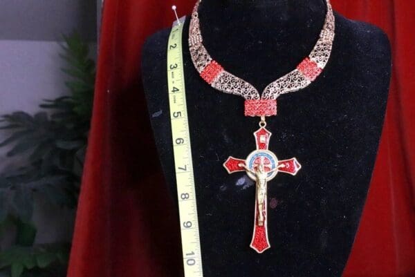 A cross necklace is shown on display in front of a measuring tape.