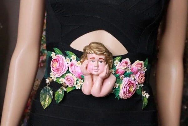 A woman wearing a black dress with pink flowers and a cherub.