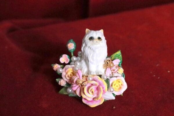 A white cat figurine sitting on top of flowers.