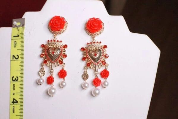 A pair of red earrings with white pearls and flowers.