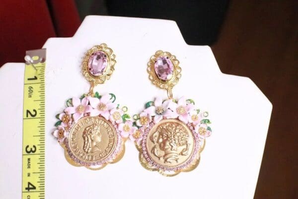 A pair of earrings with pink flowers and gold coins.