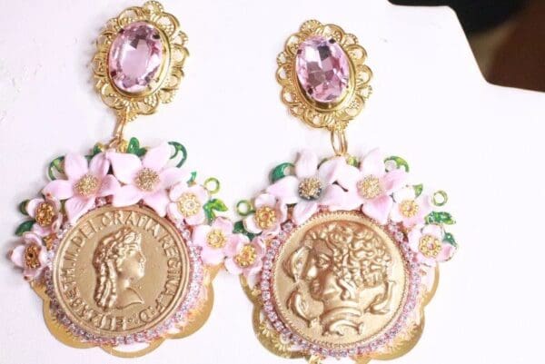 A pair of earrings with gold coins and pink flowers.