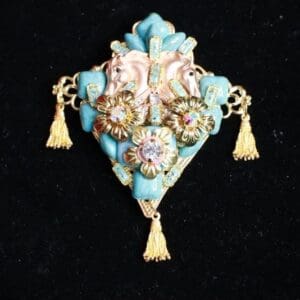 A blue and gold brooch with tassels hanging from it.