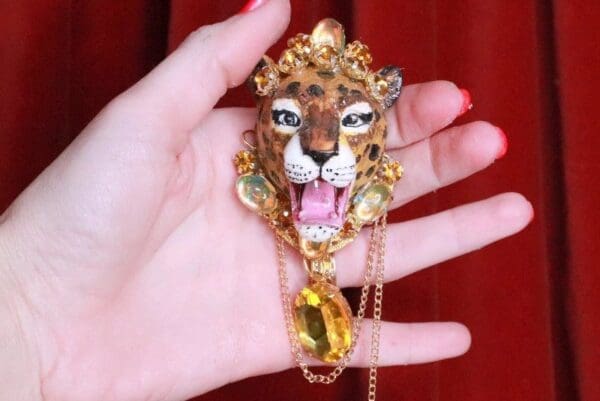 A hand holding a leopard necklace with a yellow stone.