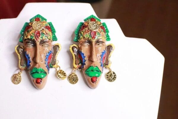 A pair of earrings with faces and ornaments on them.