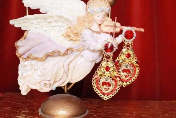 A white angel with red and gold earrings on top of it.