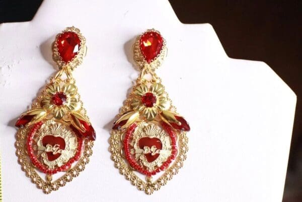 A pair of red and gold earrings on top of a white surface.