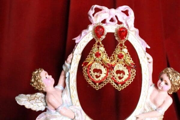 A pair of red and gold earrings sitting on top of a white frame.