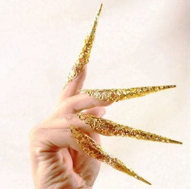 A person 's hand with long nails and gold paint.