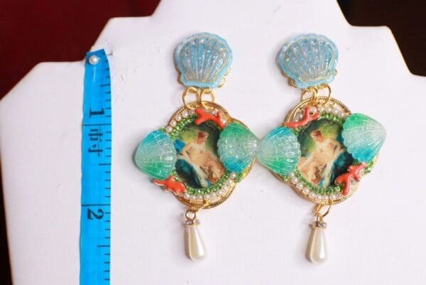 A pair of earrings with shells and a parrot on them.