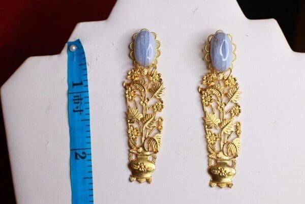 A pair of gold earrings with blue stone on top.