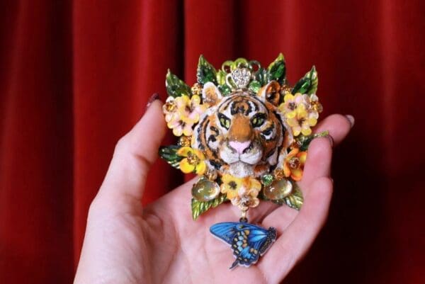 A hand holding up a tiger and butterfly brooch.