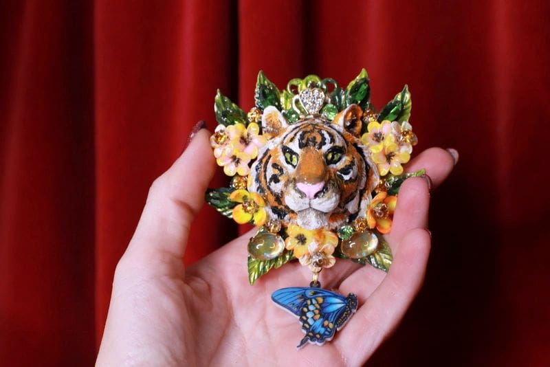 A hand holding up a tiger and butterfly brooch.