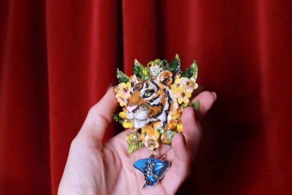 A hand holding a tiger and butterfly pin.
