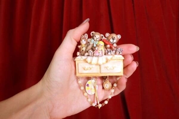A hand holding a box of jewelry in front of red curtain.