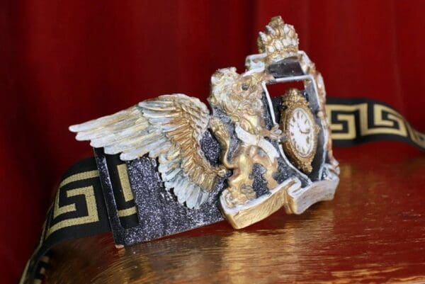 A clock with wings and gold paint on top of a table.