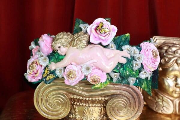 A statue of a cherub with pink flowers on top.