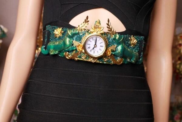 A woman wearing a black dress and green belt with gold embellishments.