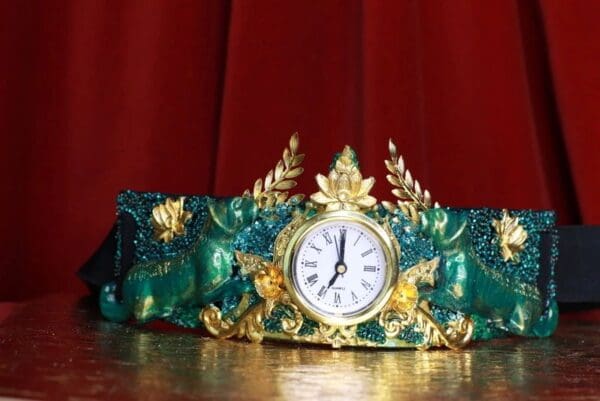 A clock is sitting on the table in front of a red curtain.