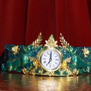 A clock is sitting on the table in front of a red curtain.