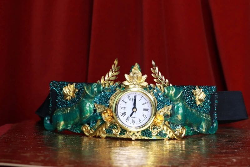 A clock is sitting on the table in front of a red curtain.