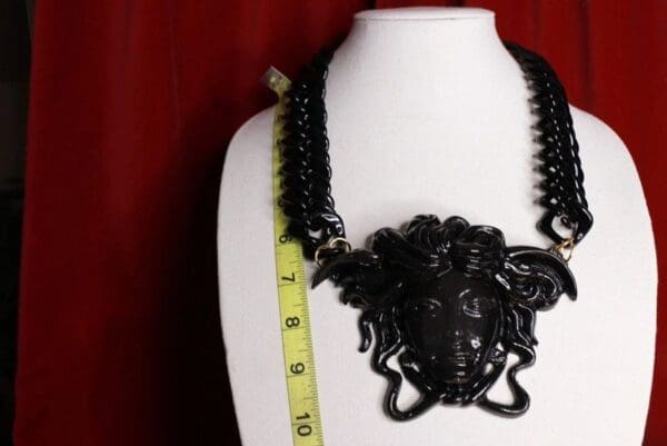 A black necklace with a large medusa head on it.
