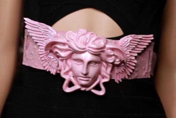 A pink winged medusa head on top of a black background.