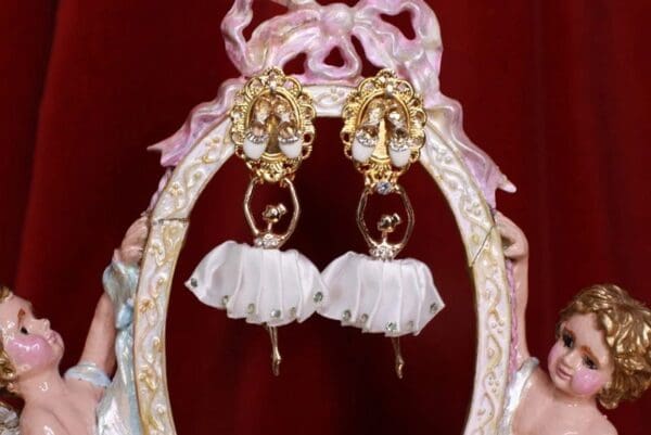 A pair of earrings with white fabric and gold frame.