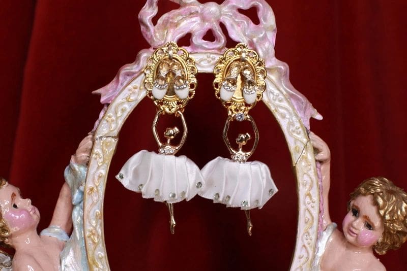A pair of earrings with white fabric and gold frame.