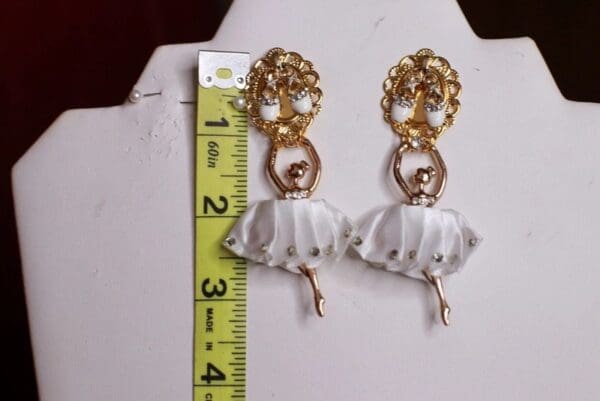 A pair of earrings with a gold chain and white fabric.