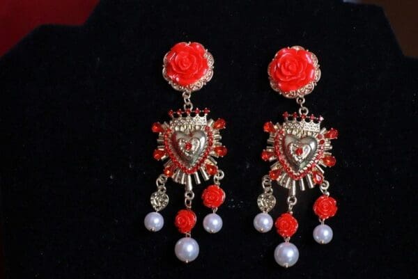 A pair of earrings with red roses and pearls.