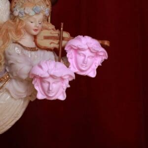 A pink statue of two faces holding strings.