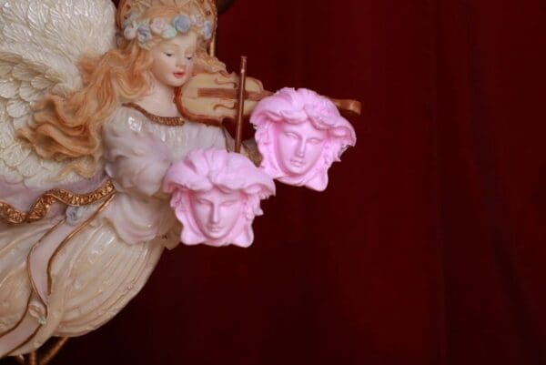 A pink statue of two faces holding strings.