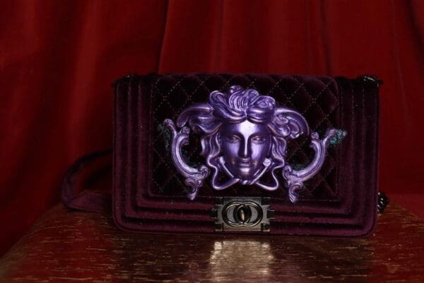 A purple purse with a medusa head on it.