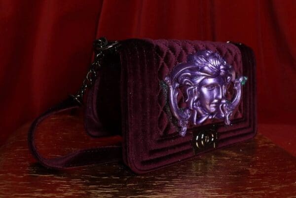 A purple purse with an image of medusa on it.