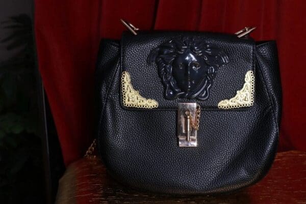 A black purse with gold accents on top of a red curtain.