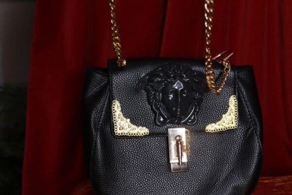 A black purse with gold chain and medusa head.